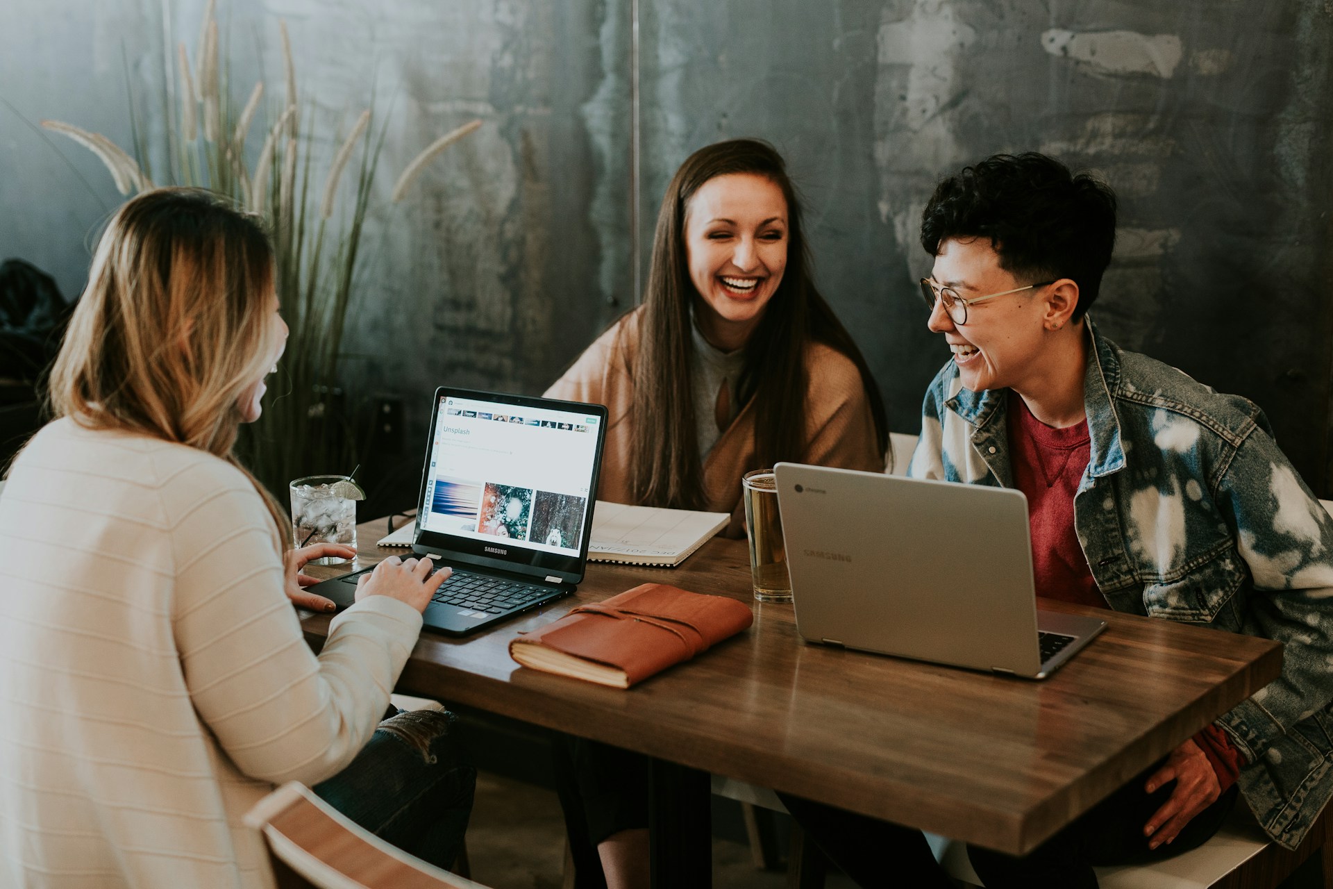 Three people laughing in front of laptops