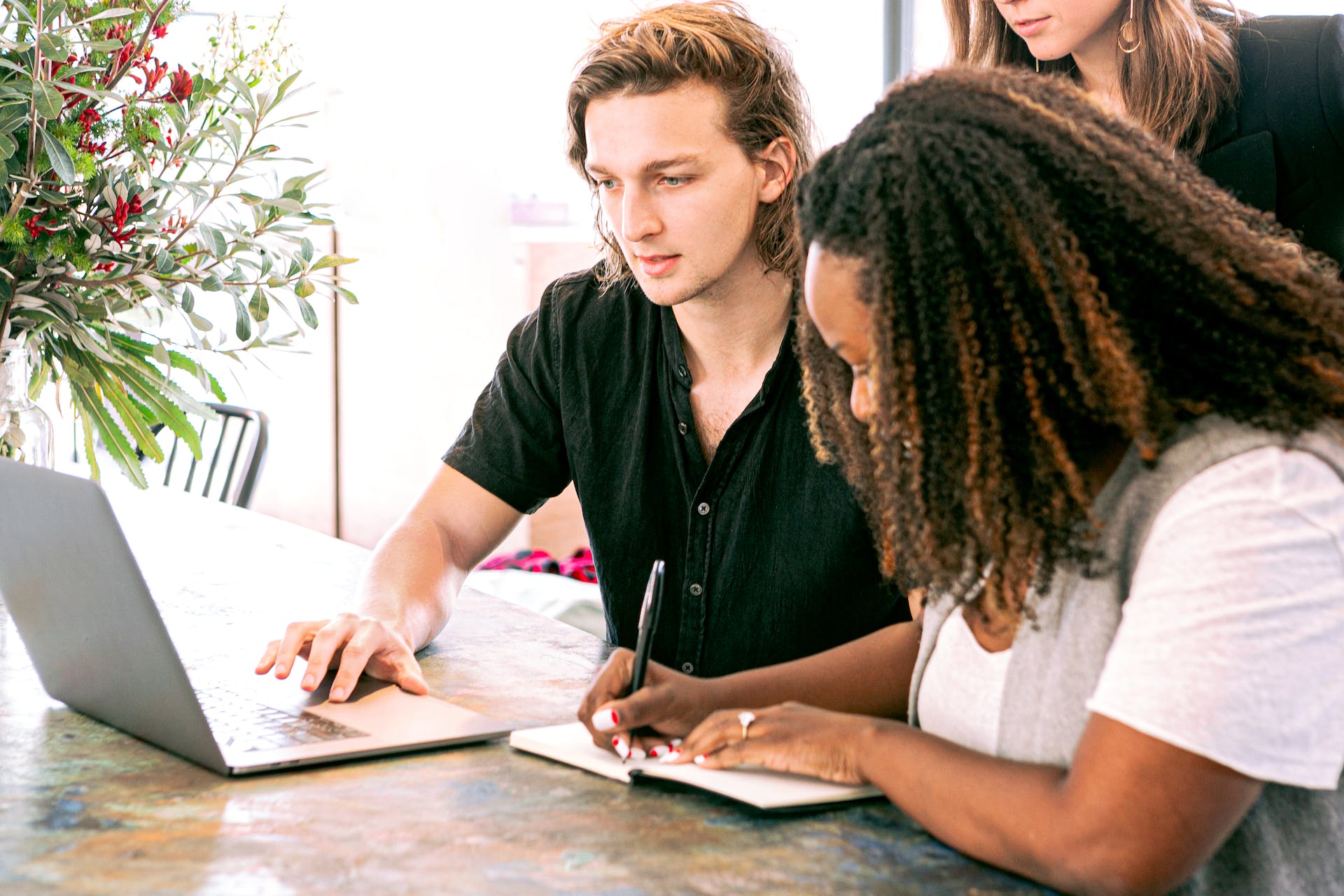 Guy Looking at Laptop While a Woman Writes Something on Notebook